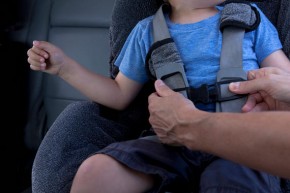 Mother fastening child safety seat belt in car